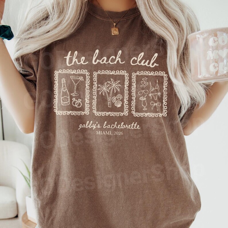 May include: A brown t-shirt with the text "the bach club" and three framed illustrations. The illustrations include a champagne bottle, cocktail, palm trees, seashells, and swimwear. The text "gabby's bachelorette, Miami, 2026" is also printed on the shirt.