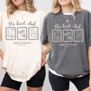 May include: Two t-shirts, one cream and one gray, with the text "the bach club" above three framed illustrations. The illustrations include a champagne bottle, a cocktail, a palm tree, and other party-themed graphics. Below the illustrations is the text "gabby's bachelorette, MIAMI, 2026."