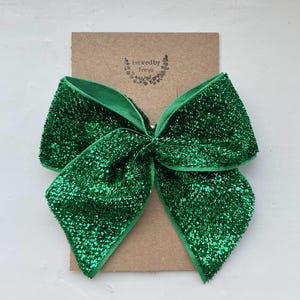 May include: A large green glitter bow with a satin finish. The bow is tied and ready to be used as a hair bow or decoration.