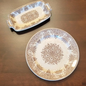 May include: Two-piece vintage serving set with a brown and white floral design. The set includes a rectangular serving dish with handles and a round dinner plate. The intricate pattern is centered on both pieces.