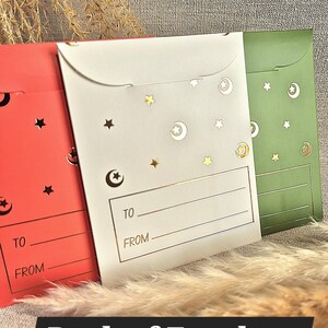 May include: Three red, white and green envelopes with gold stars and crescent moons. The envelopes have a gold line and the words "TO" and "FROM" printed on them.