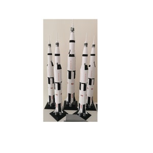 May include: Five white and black model rockets on black stands. The rockets are all the same design, with a white body and black stripes. The rockets are all about 12 inches tall.