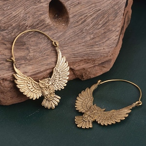 May include: A pair of gold-toned hoop earrings with an owl design. The owls have detailed wings and are facing forward.