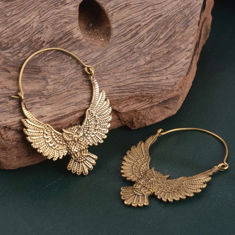 May include: A pair of gold-toned hoop earrings with an owl design. The owls have detailed wings and are facing forward.
