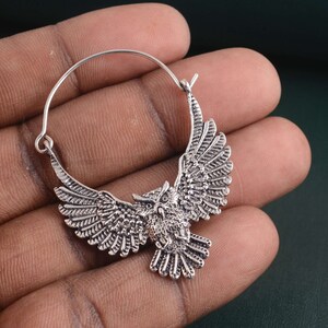 May include: Silver hoop earrings with an owl design. The owl is in flight with its wings spread wide. The earrings are made of metal and have a silver finish.
