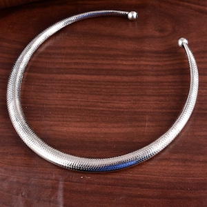 May include: A silver choker necklace with a textured surface and rounded ends.