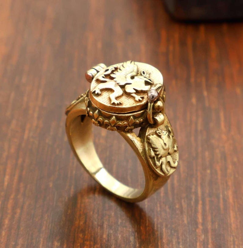 May include: A gold-colored ring with a detailed design. The ring features a lion emblem on the top and decorative elements on the band. The ring appears to be made of metal and has an antique or vintage aesthetic.