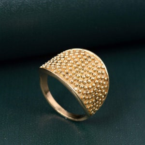 May include: A wide gold-toned ring featuring a textured surface covered in numerous small, raised spherical beads. The band has a smooth, polished interior and a curved, dome-like exterior profile that is entirely adorned with the uniform dot pattern.
