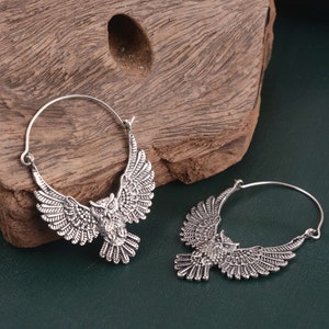 May include: A pair of silver hoop earrings with an owl design. The owls are detailed and have spread wings.
