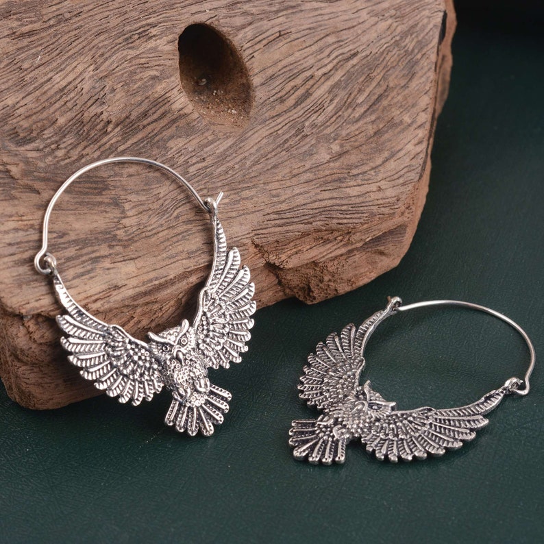 May include: A pair of silver hoop earrings with an owl design. The owls are detailed and have spread wings.