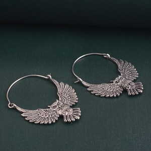 May include: A pair of silver hoop earrings with an owl design. The owls have detailed wings and are facing forward.