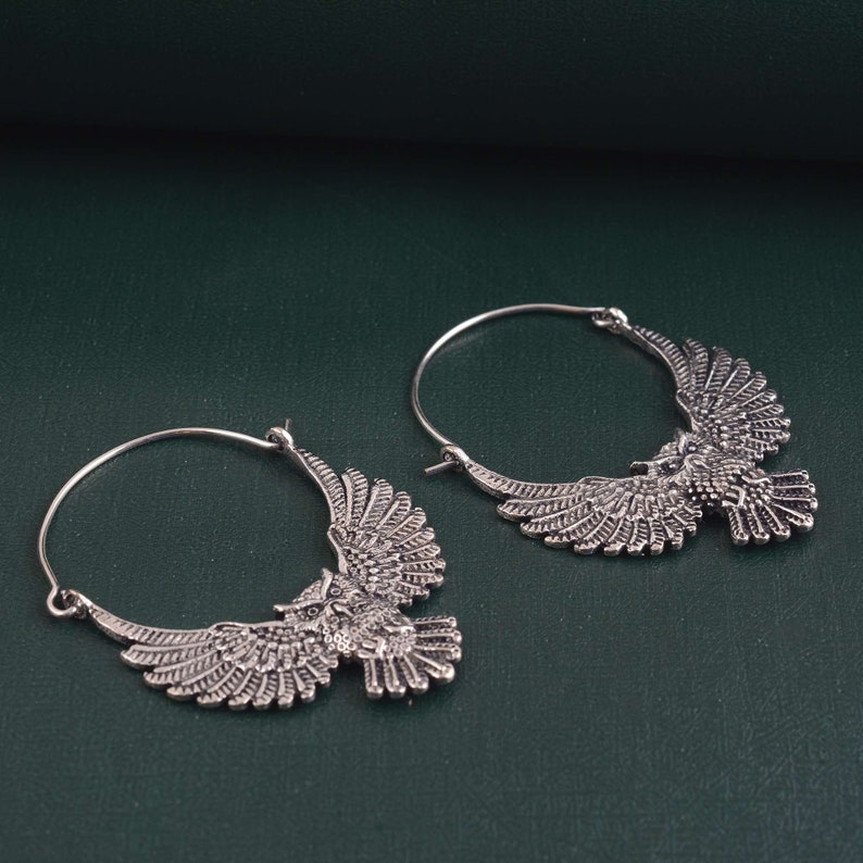 May include: A pair of silver hoop earrings with an owl design. The owls have detailed wings and are facing forward.