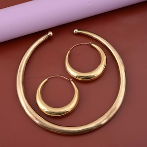 May include: A set of gold-toned hoop earrings and a matching necklace. The earrings and necklace are all made of a thick, rounded metal.
