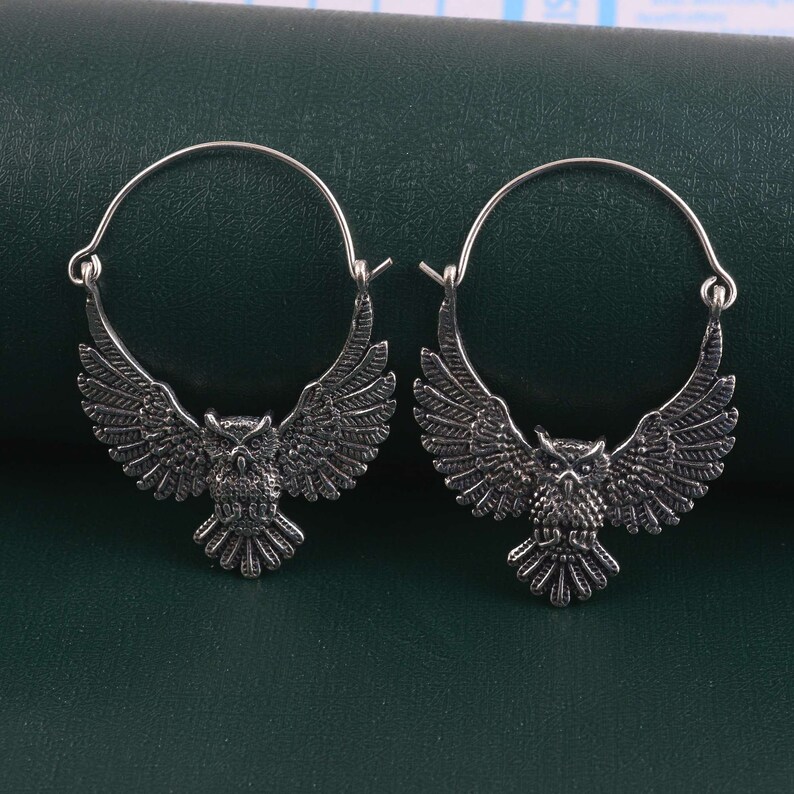 May include: A pair of silver hoop earrings with an owl design. The owls are facing forward with their wings spread out.