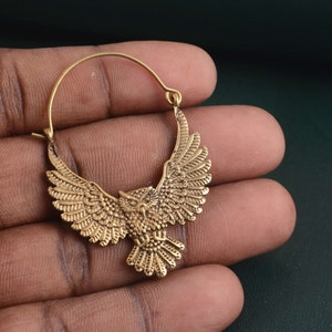 May include: Gold hoop earrings with an owl design. The owl is detailed with feathers and has its wings spread out.