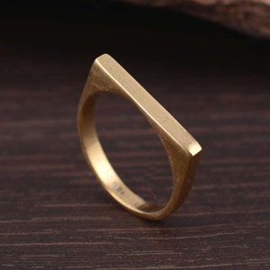 Può includere: Un anello dorato con una fascia piatta e rettangolare.