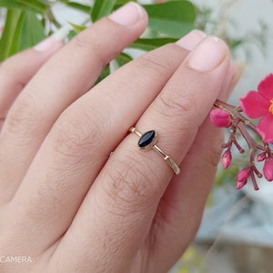 Könnte beinhalten: Ein goldener Ring mit einem schwarzen ovalen Edelstein. Der Ring befindet sich an einem Finger.