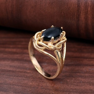 Peut inclure: Une bague en or avec une pierre précieuse ovale noire sertie dans un design délicat et complexe.