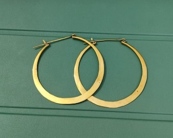 May include: A pair of gold hoop earrings with a flat, wide design. The earrings are simple and elegant.