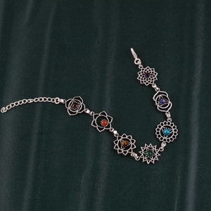 May include: Silver-toned bracelet featuring seven openwork floral designs, each with a different colored gemstone. The gemstones include red, orange, brown, green, blue, purple, and turquoise. The bracelet has a chain closure.