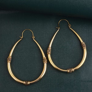May include: A pair of large, gold-toned hoop earrings with decorative accents. The earrings are oval-shaped and have a smooth, polished finish.