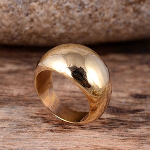 May include: A gold-colored ring with a rounded, domed top. The ring is made of metal and has a smooth, polished finish.