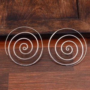 Op de afbeelding: Een paar zilveren spiraalvormige oorringen. De oorringen zijn gemaakt van dunne draad en hebben een gehamerde textuur.