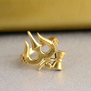 May include: A gold-colored ring with a trident design. The ring is made of metal and has a smooth finish.