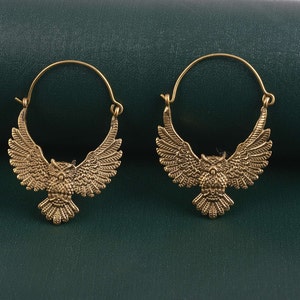 May include: A pair of gold-toned hoop earrings with an owl design. The owls have spread wings and are facing forward.
