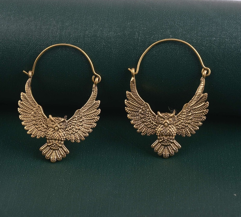 May include: A pair of gold-toned hoop earrings with an owl design. The owls have spread wings and are facing forward.