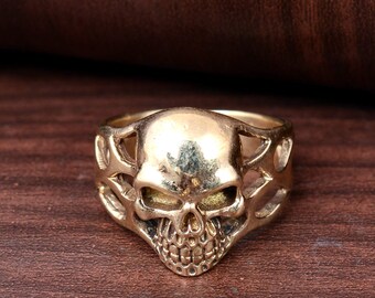 Peut inclure: Une bague en forme de crâne dorée avec un design complexe. Le crâne est détaillé avec des orbites, un nez et une bouche.