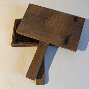 Peut inclure: Une brosse en bois avec une poignée brun foncé et une tête de brosse à poils noirs. La brosse est en position fermée, la poignée étant repliée sur la tête de brosse.