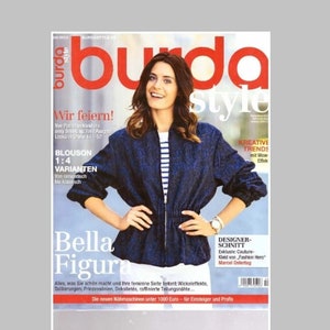 May include: A Burda Style magazine cover featuring a dark blue textured blouson jacket with a front zip, worn over a white and navy blue striped shirt and white trousers. The cover includes text such as burda style, Wir feiern, BLOUSON 1:4 VARIANTEN, Bella Figura, and KREATIVE TRENDS.