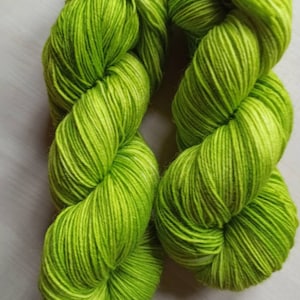 Könnte beinhalten: Zwei Stränge leuchtend grüner Wolle, eng gewickelt und nebeneinander dargestellt. Das Garn hat ein farbvariiertes Muster mit hellgrünen und weißen Highlights. Das Garn ist weich und flauschig, perfekt für Strick- oder Häkelprojekte.