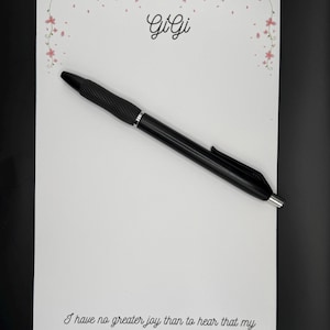 May include: A black pen rests on a white card with the name "GiGi" in cursive and a floral border. The card also features a Bible verse: "I have no greater joy than to hear that my children are walking in the truth. 3 John 1:4."