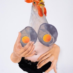 May include: A surreal collage featuring a rooster's head with a red comb and a white body. The body is adorned with two fried egg-shaped breasts and a black lace bottom. The hands are holding the eggs.