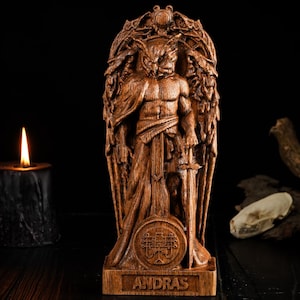 May include: A wooden statue of a figure with wings and a sword, standing on a base with the name "ANDRAS" carved on it. The statue is set against a dark background with a lit candle and a bird skull.