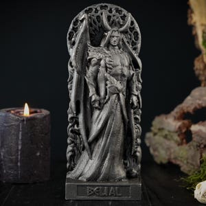May include: A detailed, gray statue of a figure with horns and a flowing robe, set against a dark background with a lit candle, moss, and animal skulls. The statue has the word "EQIAL" on its base.
