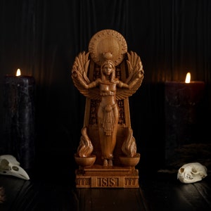 May include: A wooden statue of the Egyptian goddess Isis, standing on a base with the word "ISIS" inscribed. The statue is surrounded by black candles and white animal skulls.