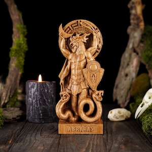May include: A wooden statue of Abraxas, a deity from ancient Gnosticism, holding a crescent moon and a shield. The statue is carved with intricate details and stands on a base with the inscription "ABRAXAS".