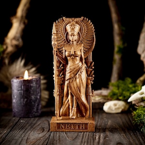 May include: Wooden statue of the Egyptian goddess Neith, standing tall with a staff and wings. The statue is carved with intricate details and has a dark brown finish. The base of the statue is inscribed with the word "NEITH".