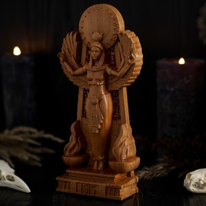 May include: A wooden statue of the Egyptian goddess Isis, standing on a base with the word "Isis" inscribed. The statue is surrounded by candles and skulls, creating a dark and mystical atmosphere.