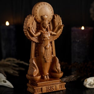 May include: A wooden statue of the Egyptian goddess Isis, standing on a base with the word "ISIS" inscribed. The statue is intricately carved with details of her wings, headdress, and clothing.