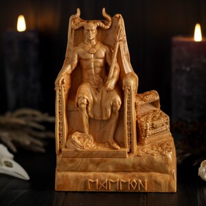 May include: Wooden statue of a demon figure sitting on a throne with a crown and a scepter. The statue is carved with intricate details and has a dark brown finish. The base of the statue is inscribed with the word "MAMMON".