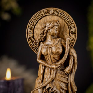 May include: A wooden carving of a woman with a crown, holding a snake. The carving is detailed and intricate, with a Greek key design around the woman's head.