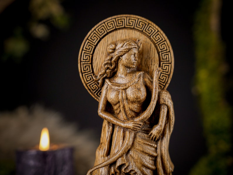 May include: A wooden carving of a woman with a crown, holding a snake. The carving is detailed and intricate, with a Greek key design around the woman's head.