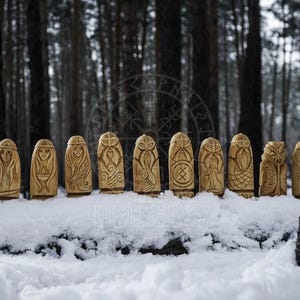 Puede incluir: Una fila de 12 figuras de madera talladas con s&iacute;mbolos de la mitolog&iacute;a n&oacute;rdica, de pie sobre una superficie nevada en un entorno boscoso.