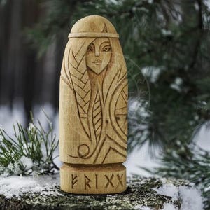 Puede incluir: Una talla de madera de una figura femenina con detalles intrincados, que incluyen un peinado trenzado y un dise&ntilde;o estilizado en el pecho. La talla est&aacute; etiquetada con "FRIXX" en la base.