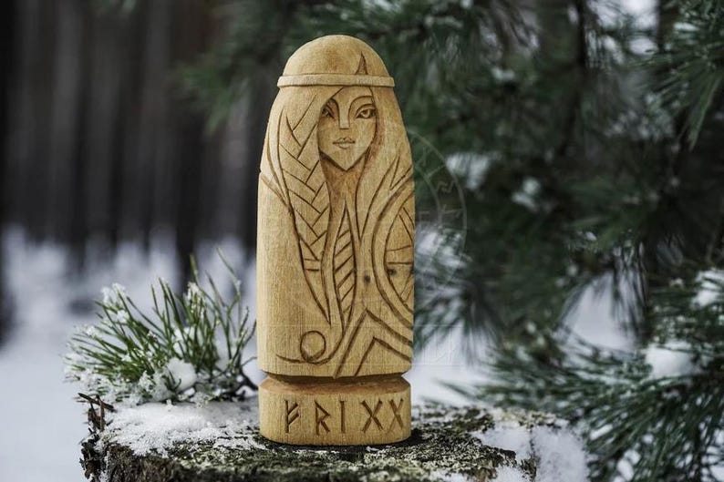 Puede incluir: Una talla de madera de una figura femenina con detalles intrincados, que incluyen un peinado trenzado y un dise&ntilde;o estilizado en el pecho. La talla est&aacute; etiquetada con "FRIXX" en la base.