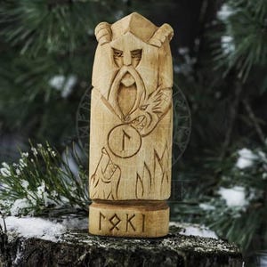 Puede incluir: Estatua de madera tallada a mano de un dios n&oacute;rdico con barba y un lobo a sus pies. La estatua est&aacute; pintada en tonos marrones y tiene un s&iacute;mbolo de runa tallado en ella. La estatua est&aacute; etiquetada como "Loki" en runas.
